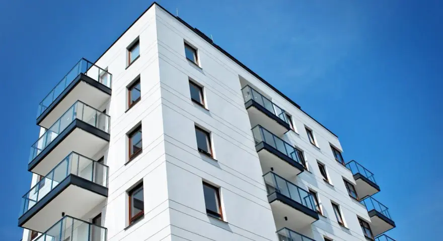 Nowoczesny budynek mieszkalny z balkonami i szklanymi balustradami, na tle błękitnego nieba. Idealne miejsce do życia, jak w pit 39.