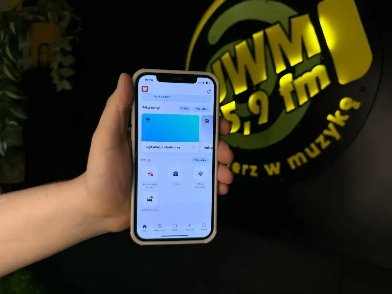 Dłoń trzyma smartfon z widoczną aplikacją mobilną, gdzie można znaleźć legitymację studencką. To cyfrowy dowód statusu studenta.