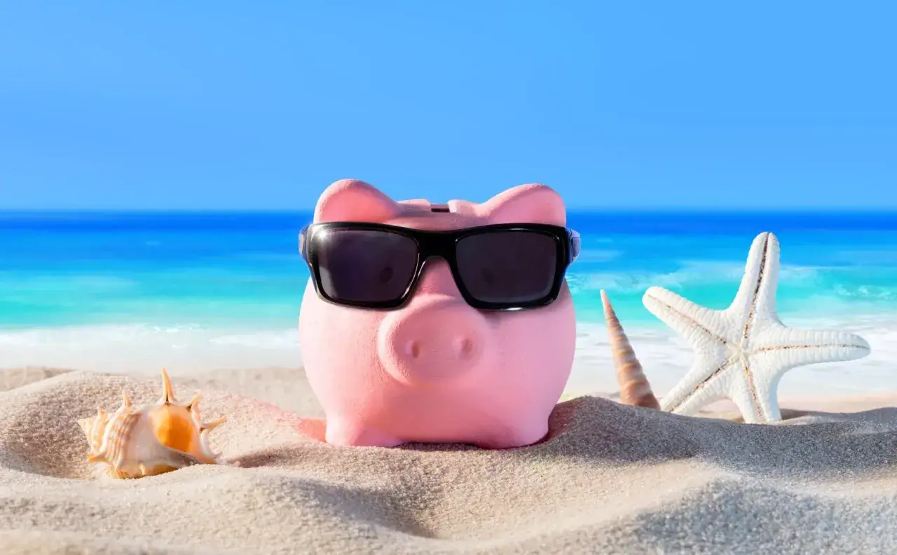 Różowa świnka-skarbonka w okularach przeciwsłonecznych odpoczywa na plaży. Obok niej muszelki i rozgwiazda. To idealne wczasy pod gruszą!