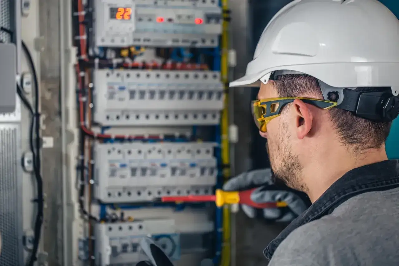 Elektryk w kasku i okularach ochronnych pracuje przy rozdzielnicy. Zastanawiasz się, ile zarabia elektryk?