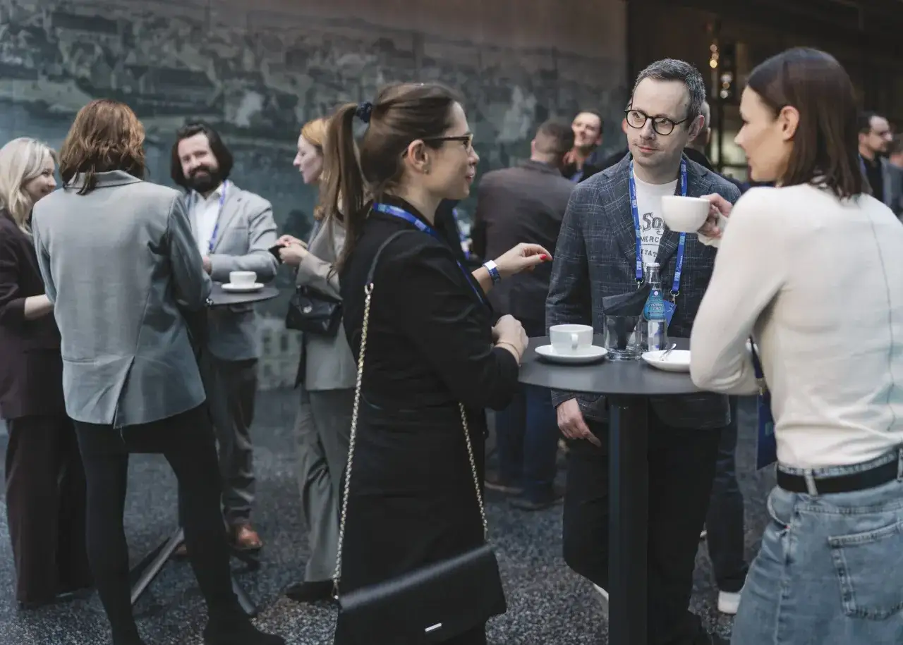 Ludzie rozmawiają przy stolikach, pijąc kawę. To przykład networking, czyli budowania relacji biznesowych.